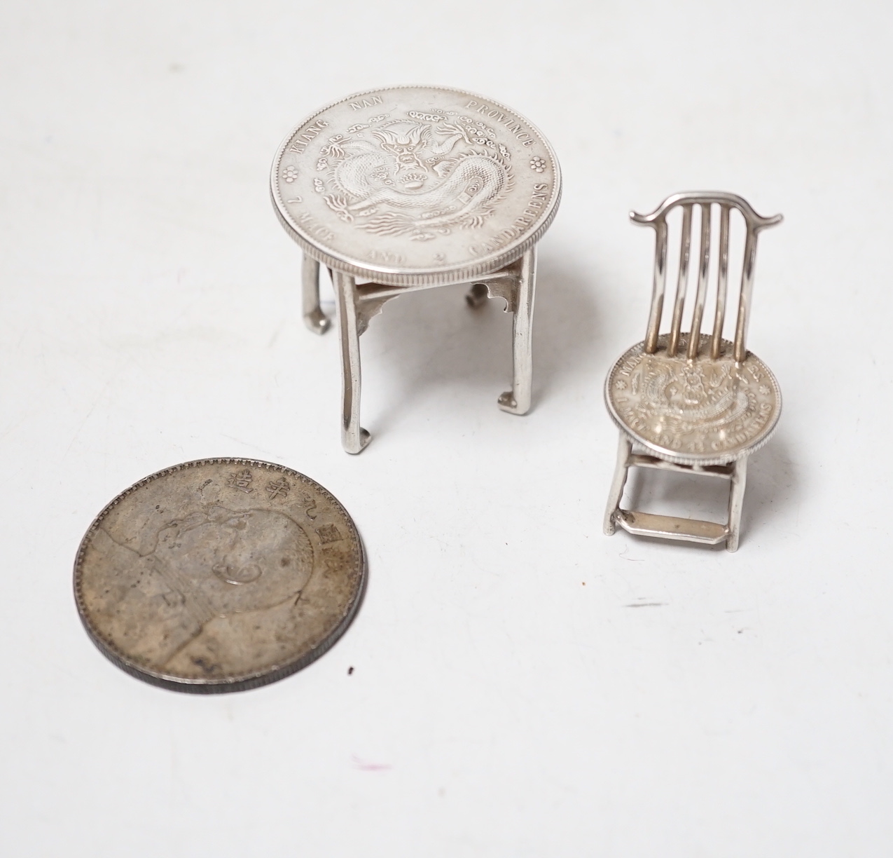 A Chinese Republic period one dollar 1920, and two Chinese Guangxu period coins mounted as miniature furniture, table 4vm higher